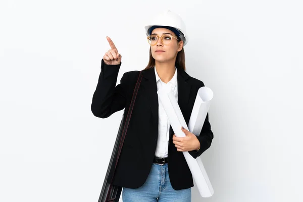 Young architect caucasian woman with helmet and holding blueprints over isolated background touching on transparent screen