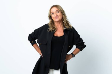 Orta yaşlı sarışın kadın soyutlanmış beyaz arka planda kolları kalçasında ve gülümsüyor.