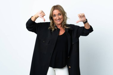 Orta yaşlı sarışın kadın soyutlanmış beyaz arka planda iki eliyle baş parmağını gösteriyor.