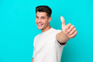 Genç, yakışıklı, beyaz bir adam, mavi bir bakkalda izole edilmiş bir şekilde baş parmak işareti yapıyor.