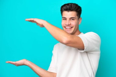 Genç, beyaz, yakışıklı bir adam, mavi bir bakkal sahasında izole edilmiş. Kopyalama alanı olan bir ilan vermek için.