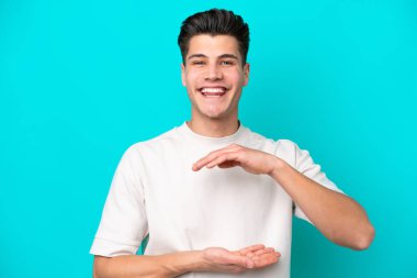 Mavi fırında izole edilmiş yakışıklı beyaz bir adam. Elinde bir ilan vermek için avucunun içinde hayali bir fotokopi makinesi tutuyor.