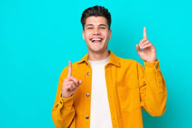 Young handsome caucasian man isolated on blue bakcground pointing up a great idea