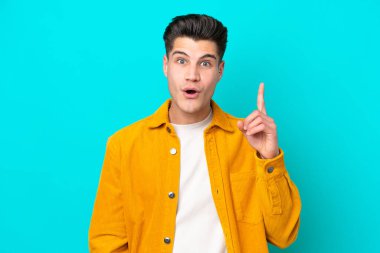 Genç yakışıklı beyaz adam mavi bakkalda izole edilmiş. Çözümü bulmak için parmağını kaldırıyor.