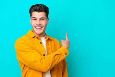Young handsome caucasian man isolated on blue bakcground pointing back