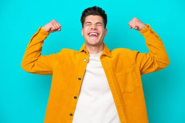 Genç, yakışıklı, beyaz bir adam, mavi bakkaldan izole edilmiş, güçlü bir jest yapıyor.