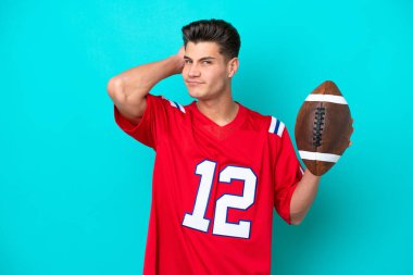 Rugby oynayan Kafkasyalı genç adam mavi arka planda izole edilmiş. Şüpheleri var.