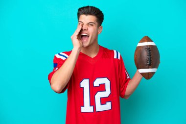 Rugby oynayan beyaz bir adam mavi arka planda izole edilmiş ve ağzı açık bağırıyor.