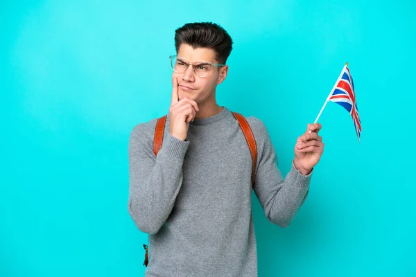 Mladý Běloch Drží Vlajku Spojeného Království Izolovanou Modrém Pozadí Pochybnostmi — Stock fotografie