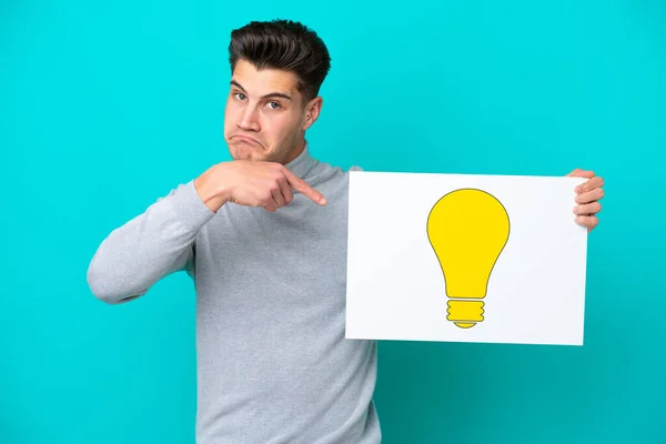 Young Handsome Caucasian Man Isolated Blue Bakcground Holding Placard Bulb — Stock Photo, Image