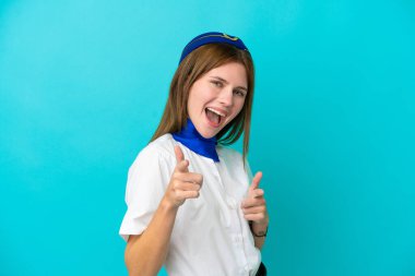 Uçak hostesi İngiliz kadın mavi arka planda izole edilmiş ön tarafı işaret ediyor ve gülümsüyor.