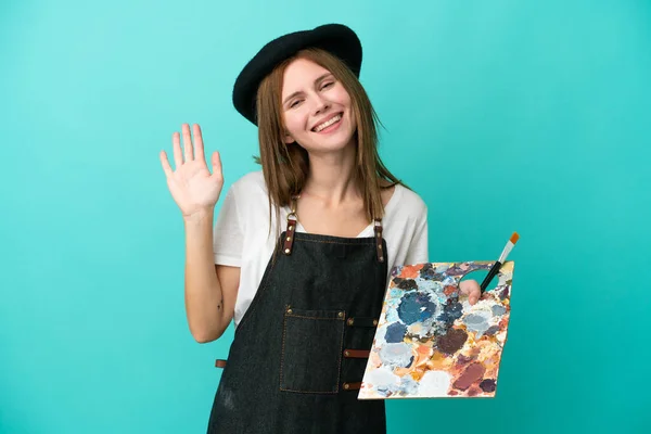 Młoda Artystka Angielka Trzyma Paletę Odizolowanych Niebieskim Tle Salutując Ręką — Zdjęcie stockowe