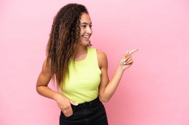 Pembe arka planda izole edilmiş genç bir İspanyol kadın parmak göstererek bir ürün sunuyor.
