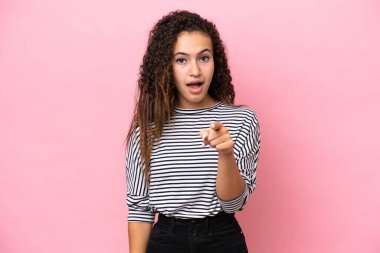 Pembe arka planda izole edilmiş genç İspanyol kadın şaşırmış ve ön tarafı işaret ediyor.