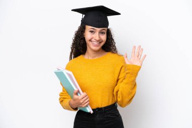 Arap üniversitesinden mezun bir kadın elinde kitaplarla beyaz arka planda mutlu bir ifadeyle selam veriyor.