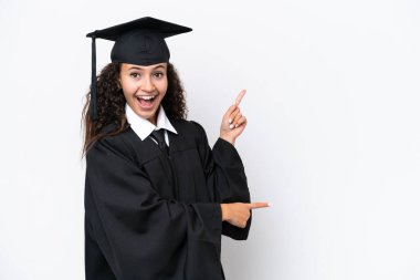 Genç üniversite mezunu, beyaz arka planda izole edilmiş, şaşırmış ve işaret eden Arap kadın.