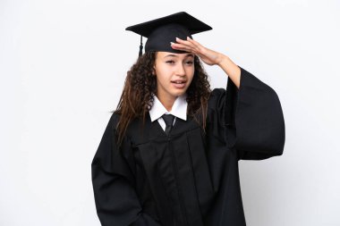 Üniversite mezunu genç bir Arap kadın beyaz arka planda izole bir şekilde bir şeye bakmak için uzaklara bakıyor.