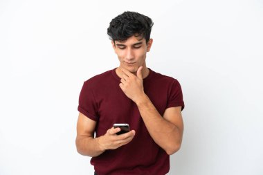 Genç Arjantinli adam beyaz arka planda izole edilmiş düşünüyor ve bir mesaj gönderiyor.
