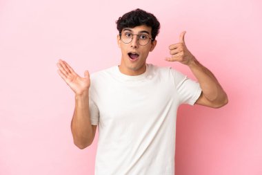 Arjantinli genç bir adam pembe arka planda izole edilmiş telefon jestleri yapıyor.