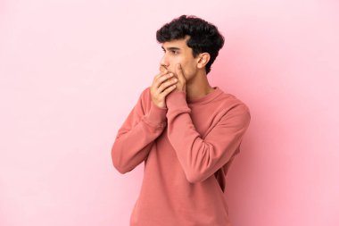 Arjantinli genç adam pembe arka planda izole edilmiş ağzını kapatıyor ve yan tarafa bakıyor.