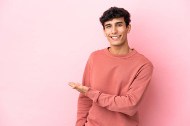 Pembe arka planda izole edilmiş genç Arjantinli adam davet edilmek için ellerini yana uzatıyor.