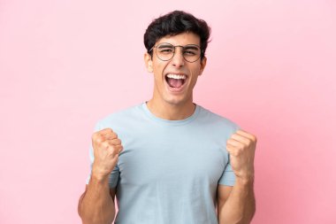Arjantinli genç bir adam pembe arka planda gözlüklü ve zaferi kutluyor.