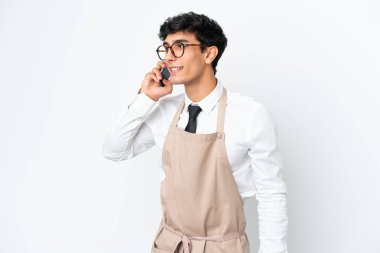Arjantinli bir restoran garsonu beyaz arka planda izole edilmiş cep telefonuyla sohbet ediyor.