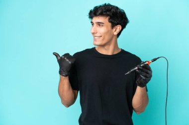 Dövme sanatçısı Arjantinli adam mavi arka planda izole edilmiş bir ürün sunmak için kenarı işaret ediyor