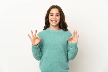 Beyaz arka planda izole edilmiş küçük beyaz kız iki eliyle tamam işareti gösteriyor.