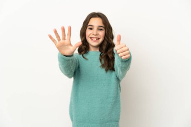 Beyaz arka planda izole edilmiş küçük beyaz kız parmaklarıyla altısını sayıyor.