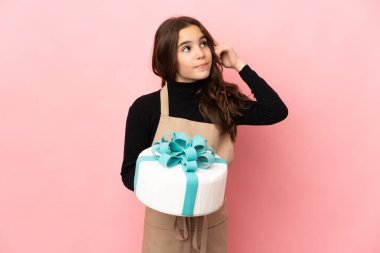 Küçük pasta şefi pembe arka planda izole edilmiş büyük bir pasta tutuyor. Şüpheleri var ve düşünüyor.
