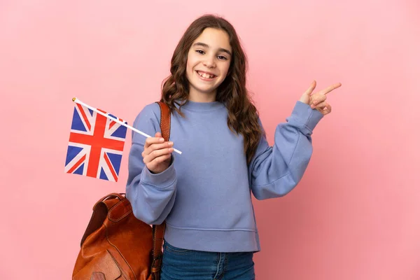 小女孩拿着一面英国国旗 用粉红的背景隔开 手指指向侧面 — 图库照片