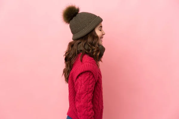 戴着冬帽的小女孩被粉色背景隔离在一边笑着 — 图库照片