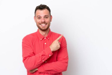 Beyaz arka planda izole edilmiş genç Brezilyalı bir adam bir ürün sunmak için kenarı işaret ediyor