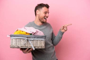 Genç Brezilyalı bir adam pembe arka planda izole edilmiş bir çamaşır sepetini tutuyor. Parmakla göstererek bir ürün sunuyor.