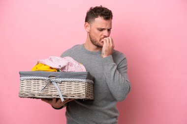 Genç Brezilyalı bir adam pembe arka planda izole edilmiş bir çamaşır sepeti tutuyor. Şüpheleri var.