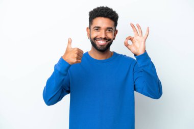 Beyaz arka planda izole edilmiş genç Brezilyalı adam işaret ve baş parmak hareketi gösteriyor.