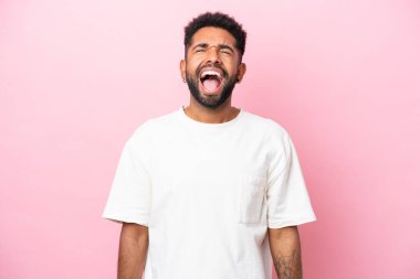 Pembe arka planda izole edilmiş genç Brezilyalı adam ağzı açık bağırıyor.