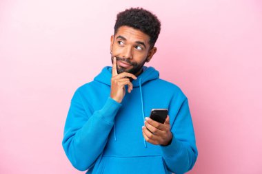 Pembe arka planda cep telefonu kullanan ve düşünen genç Brezilyalı bir adam.