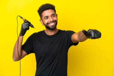 Dövme sanatçısı Brezilyalı adam sarı arka planda izole edilmiş bir şekilde baş parmak hareketi yapıyor.