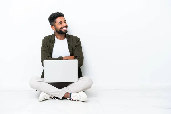 一个拿着笔记本电脑的巴西年轻人坐在地板上 被白色的快乐和微笑隔离着 — 图库照片