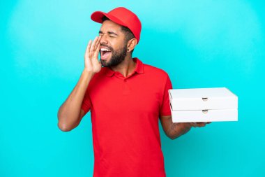 İş üniformalı Brezilyalı bir adam mavi arka planda izole edilmiş pizza kutularını topluyor ve ağzı sonuna kadar açık bağırıyor.