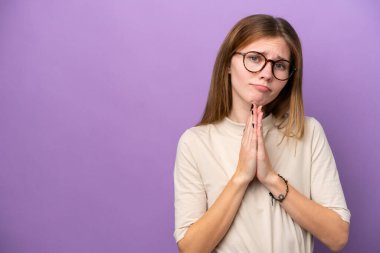 Mor arka planda izole edilmiş genç İngiliz kadın avuç içlerini bir arada tutuyor. İnsan bir şey ister.