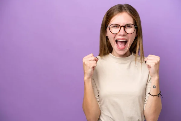 紫の背景に孤立した若い英語の女性は勝者の位置で勝利を祝う — ストック写真