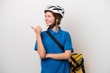 Beyaz arka planda izole edilmiş termal çantalı genç İngiliz kadın bir ürünü sunmak için kenarı işaret ediyor.