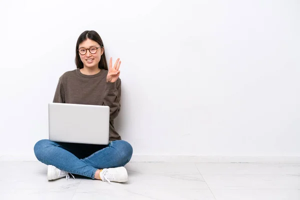 年轻的女人带着笔记本电脑快乐地坐在地板上 用手指数着三声 — 图库照片