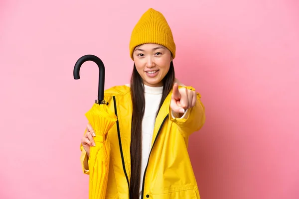 Mladá Číňanka Nepromokavým Pláštěm Deštníkem Izolované Růžovém Pozadí Ukazuje Dopředu — Stock fotografie