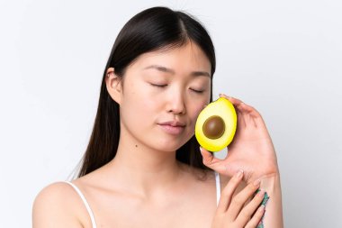 Beyaz arka planda avakado tutan genç Çinli bir kadın. Portreyi kapat