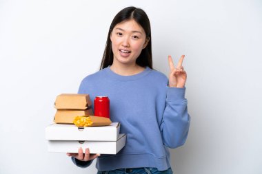 Beyaz arka planda hazır yemek tutan genç Çinli kadın gülümsüyor ve zafer işareti gösteriyor.