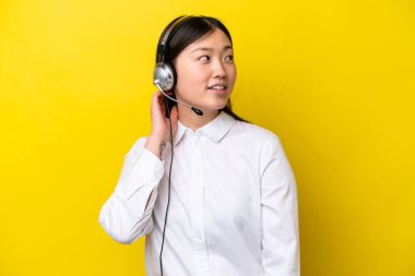 Tele pazarlamacı Çinli kadın sarı arka planda izole edilmiş bir kulaklıkla çalışıyor.